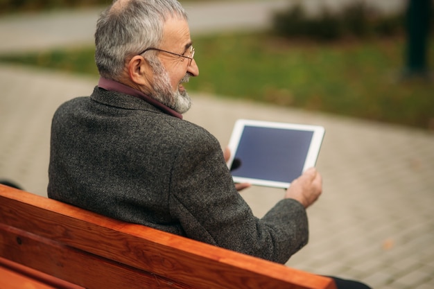 Il nonno usa un tablet seduto nel pakr sulla panchina