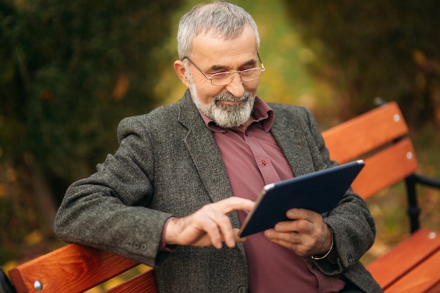 Il nonno usa un tablet seduto nel pakr sulla panchina