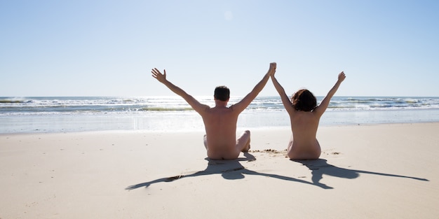 Il nudo felice delle coppie del nudista si siede sulla spiaggia del naturismo nelle vacanze estive