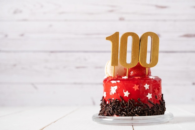 Il numero cento su una torta di compleanno rossa su sfondo chiaro