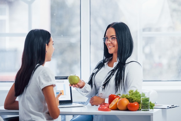 Il nutrizionista femminile con il computer portatile dà la consultazione al paziente all'interno dell'ufficio.