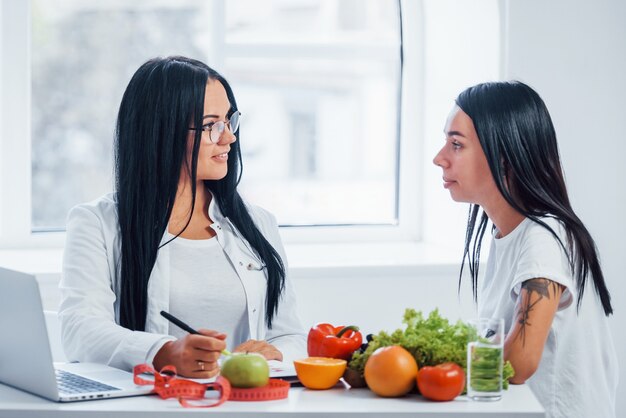 Il nutrizionista femminile con il computer portatile dà la consultazione al paziente all'interno dell'ufficio.