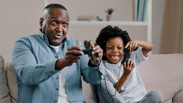 Il padre afroamericano maturo con la piccola figlia che gioca ai videogiochi sulla console usa il joystick