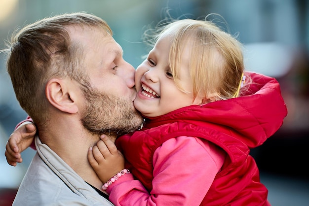 Il padre bacia la figlia sorridente all'aperto genitore maturo con il bambino