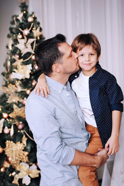 Il padre bello bacia suo figlio divertente vicino all'albero di Natale a casa