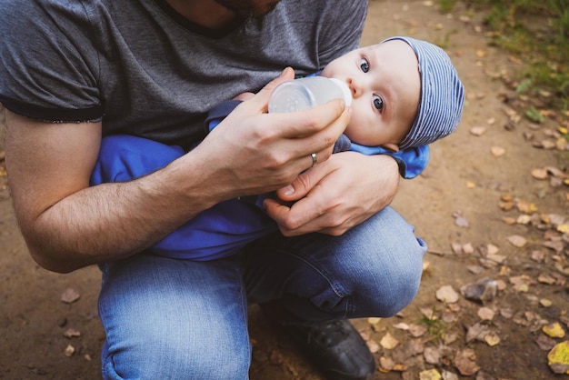 Il padre dà al figlio neonato il latte da una bottiglia all'aperto