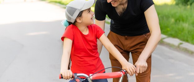 il padre di famiglia felice insegna alla figlia del bambino ad andare in bicicletta nel parco in natura.