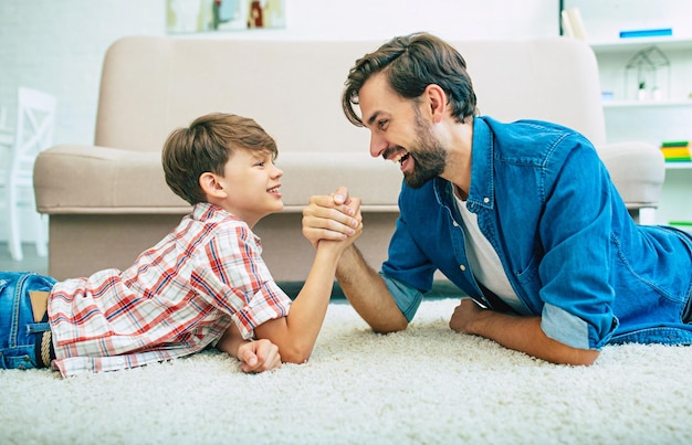 Il padre felice bello e suo figlio sorridente sono sdraiati sul pavimento a casa insieme