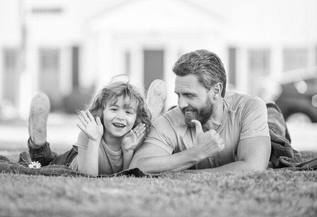 Il padre felice con il figlio si rilassa insieme sull'erba verde del parco mostra il pollice sull'amore della famiglia