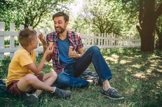 Il padre felice è seduto accanto a suo figlio sulla coperta e gli sorride. Sia lui che il bambino hanno gelati. I ragazzi si divertono a passare del tempo insieme.