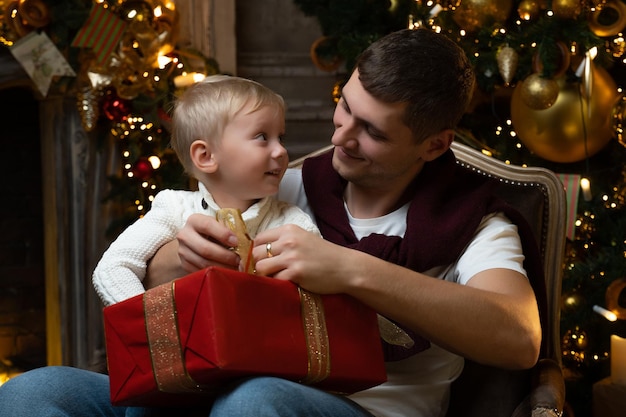 Il padre felicissimo abbraccia il suo affascinante figlioletto la famiglia festeggia il natale apre i regali si siede su un