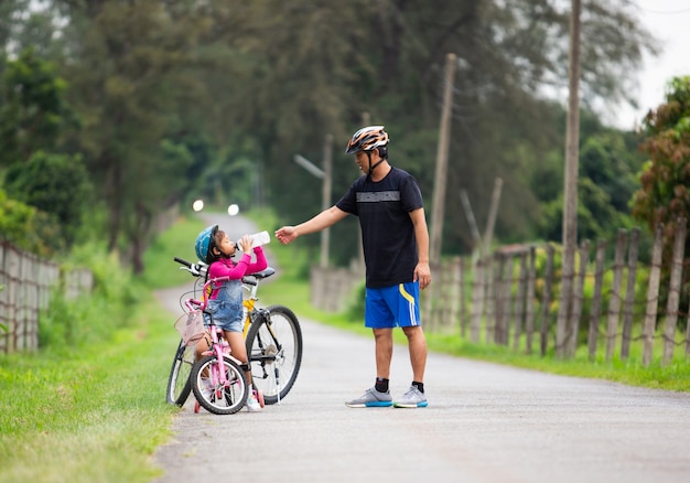 Il padre ha lasciato che sua figlia bevesse acqua mentre andava in bicicletta nel parco