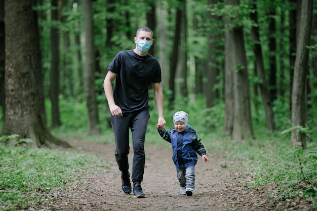 Il padre in una mascherina medica con un bambino cammina nel parco