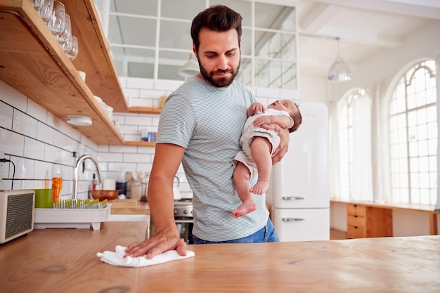 Il padre multitasking tiene il figlio del bambino addormentato e pulisce in cucina