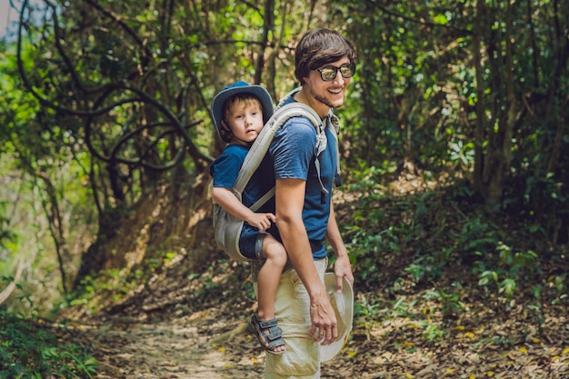 Il padre porta suo figlio in un bambino che trasporta sta facendo un'escursione nella foresta. Il turista sta portando un bambino sulla schiena nella natura del Vietnam.