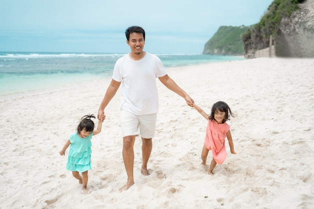 Il padre si tiene per mano due figlia sulla spiaggia