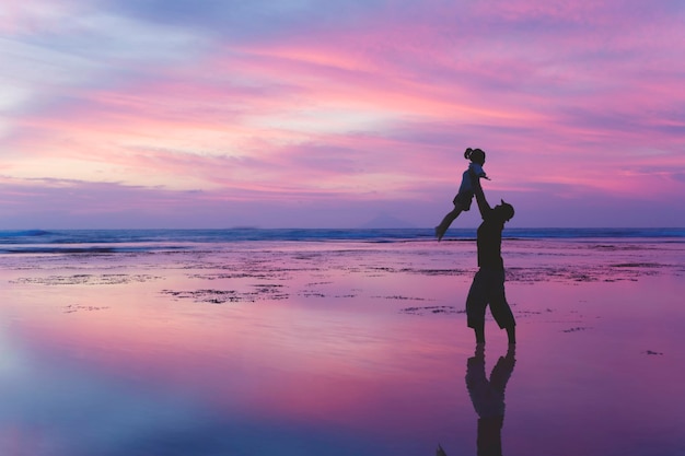 Il padre solleva sua figlia sulla spiaggia al crepuscolo