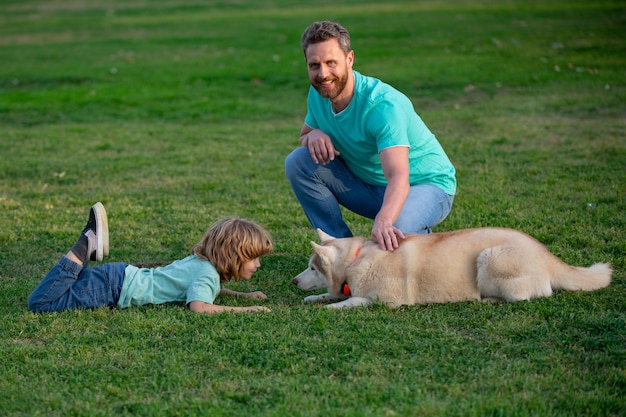 Il padre sorridente e suo figlio che giocano con il cane nel parco con il bambino dell'animale domestico camminano con il cagnolino