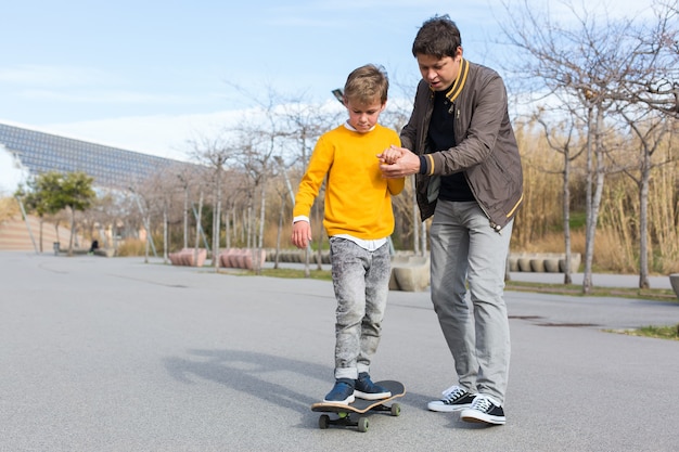 Il padre sta insegnando a suo figlio a cavalcare uno skateboard all'aperto