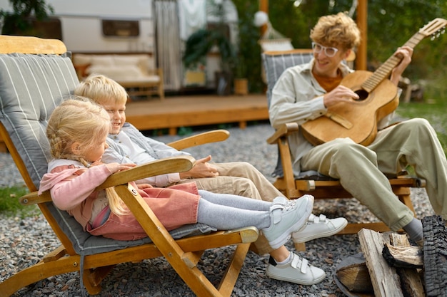 Il padre suona la chitarra per i bambini in roulotte, in campeggio