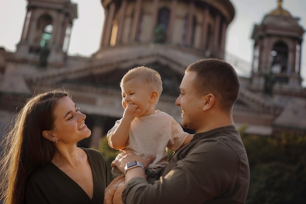 il padre tiene in braccio la madre del bambino che sta vicino a loro sorridendo e guardando felicemente il loro figlio