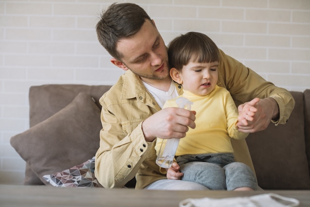 Il padre usa il disinfettante per le mani sulle mani del figlio