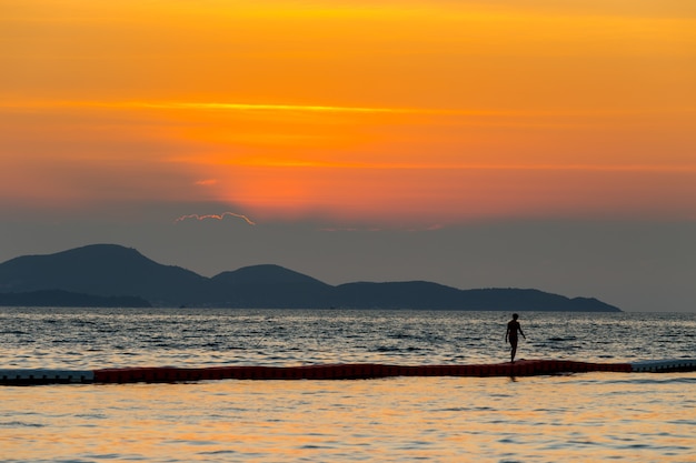 Il paesaggio del mare e un turismo femminile camminano sulla schiuma nel mare con l'ora del tramonto, Pattaya Thailandia