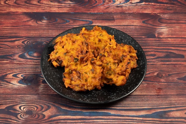 Il pakora o il pakoda di verdure speziato indiano è servito in un piatto isolato sulla vista del piano del tavolo