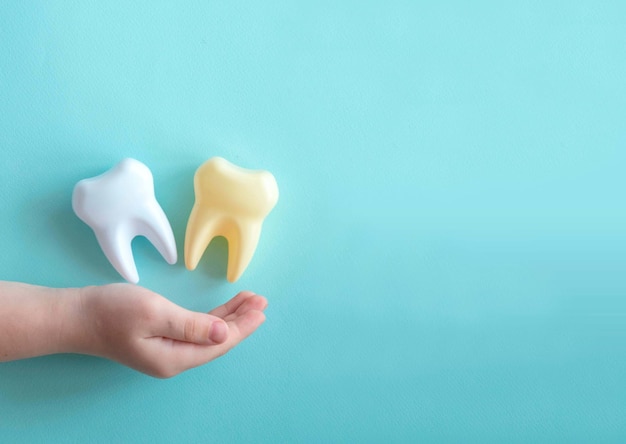 Il palmo del bambino e i grandi denti di plastica sul concetto di odontoiatria pediatrica blu