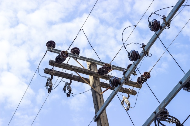 Il palo elettrico si collega ai cavi elettrici ad alta tensione su contro il cielo blu luminoso