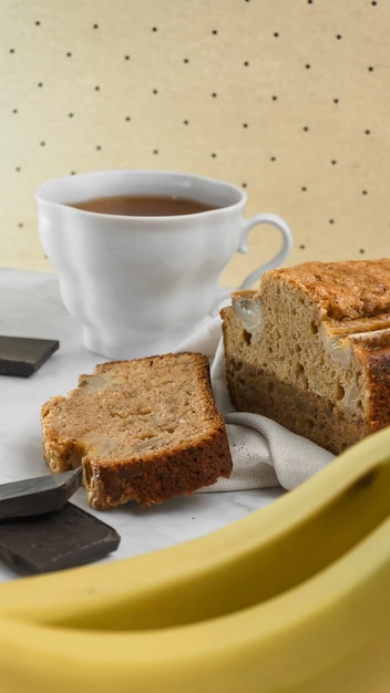 il pane alla banana si trova su uno sfondo luminoso circondato da ingredienti per cucinare e una tazza di tè