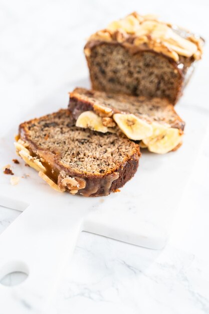 Il pane alle noci di banana affettato ha spruzzato caramello fatto in casa su un tagliere di marmo.