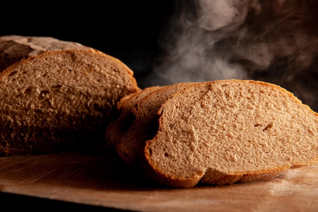 Il pane caldo tagliato a pezzi poggia su una tavola di legno su uno sfondo nero Il pane caldo viene a vapore