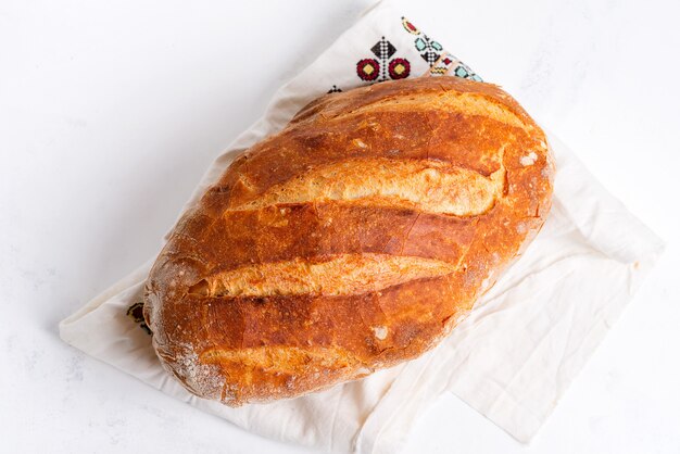 Il pane fatto in casa appena sfornato sul tavolo di marmo grigio chiaro ha decorato l'asciugamano del tessuto.