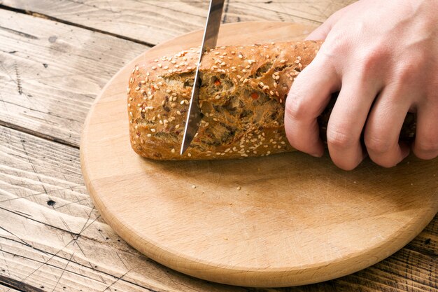 Il pane fresco con semi di girasole, semi di sesamo e lino viene tagliato a pezzi su un tagliere.