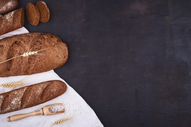 Il pane rasenta il legno con il fondo dello spazio della copia. Pani interi marroni e bianchi composizione di natura morta con spighe di grano sparse intorno. Concetto di negozio di alimentari e alimentari.