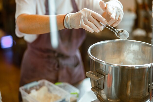 Il panettiere in guanti versa l'ingrediente in polvere nella ciotola per fare l'impasto in officina