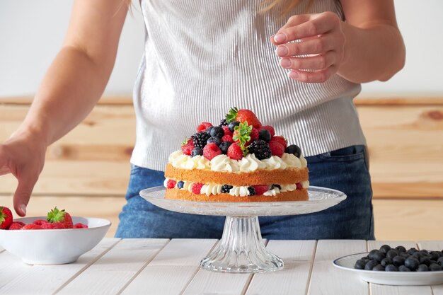 Il panettiere o la casalinga femminile decora la torta con le bacche selvatiche