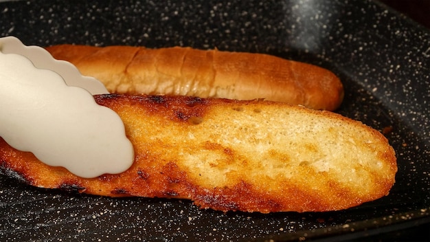 Il panino a fette per hot dog viene fritto in padella con olio da cucina fino a quando diventa croccante Preparazione di crostini fatti in casa sulla cucina domestica