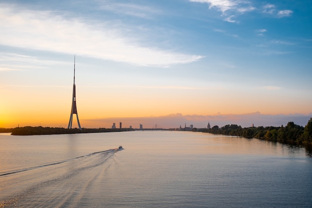 Il panorama della città vecchia di Riga e il tramonto colorato della torre della tv sul fiume daugava galleggia su una barca a motore