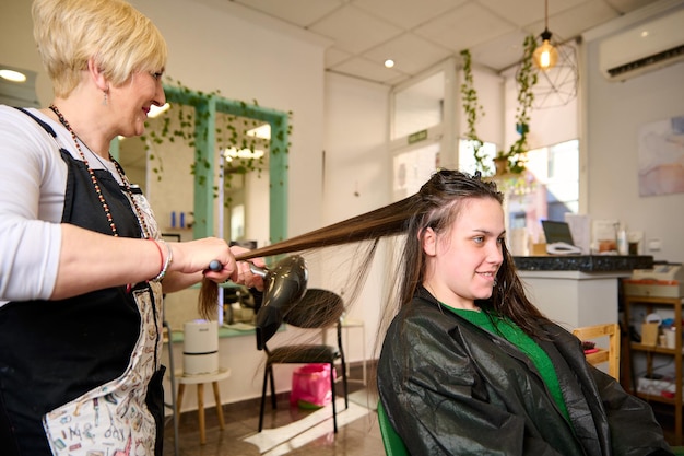 Il parrucchiere asciuga e acconcia i capelli con un asciugacapelli nel salone di bellezza