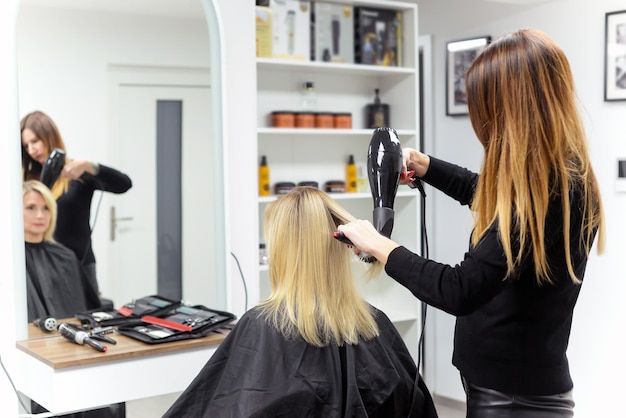 il parrucchiere asciuga i capelli con un asciugacapelli donna nel salone. close-up.beauty e concetto di moda