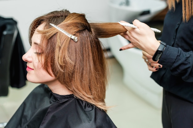 Il parrucchiere della donna sta facendo l'acconciatura alla ragazza dei capelli rossi nel salone di bellezza.