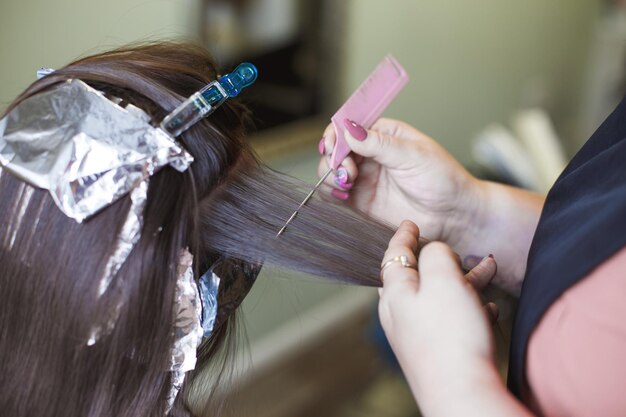 Il parrucchiere dipinge i capelli di una donna bruna nel salone di bellezza