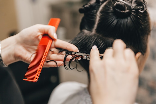 Il parrucchiere fa un taglio di capelli a una donna nel salone Il parrucchiere taglia i capelli bagnati pettinandoli con un pettine cliente con vista posteriore dei capelli corti