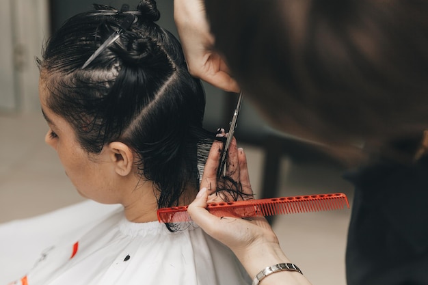 Il parrucchiere fa un taglio di capelli a una donna nel salone Il parrucchiere taglia i capelli bagnati pettinandoli con un pettine cliente con vista posteriore dei capelli corti