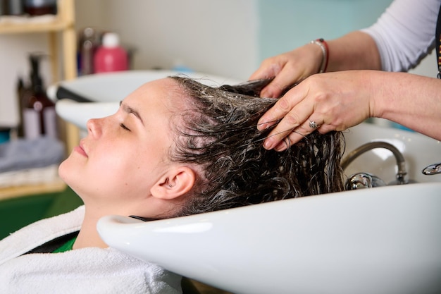 Il parrucchiere lava la testa di una ragazza bruna con lo shampoo nel salone di bellezza