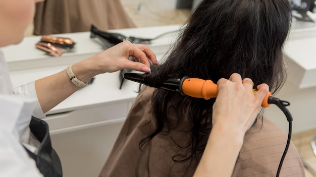 Il parrucchiere principale del salone di bellezza consente di permanente i capelli su un'acconciatura del cliente