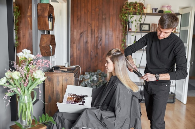 Il parrucchiere professionista sta pettinando i capelli di una bella donna bionda caucasica nel salone moderno