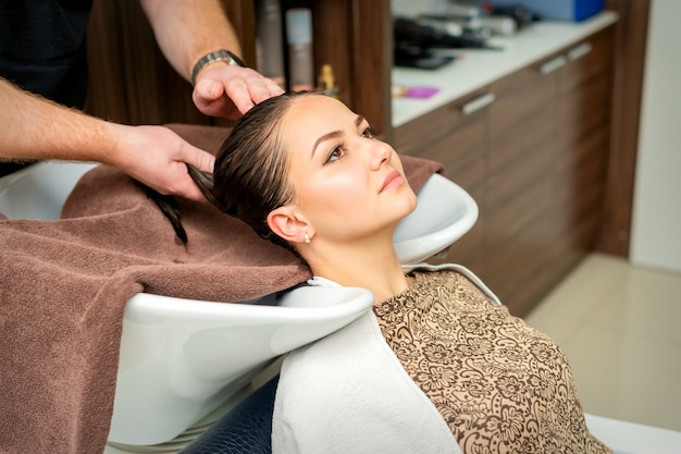 Il parrucchiere pulisce i capelli con un asciugamano di giovane donna dopo lo shampoo nel parrucchiere